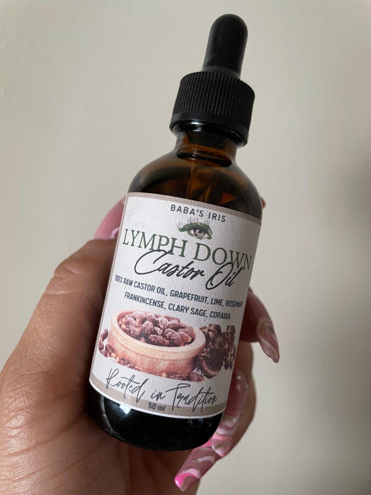 Amber dropper bottle labeled Lymph Down Castor Oil held in a hand