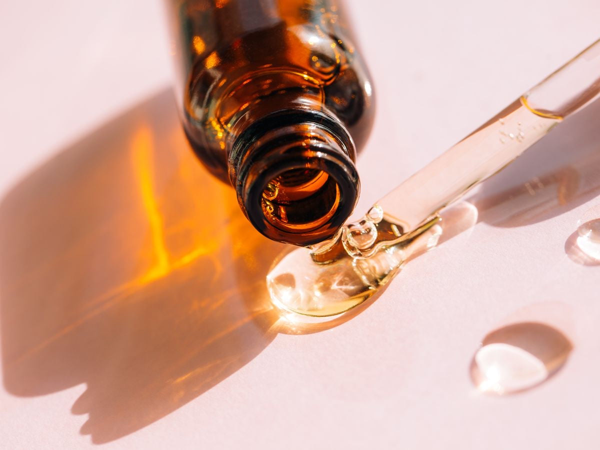 Open amber bottle with a glass dropper and oil on a white surface